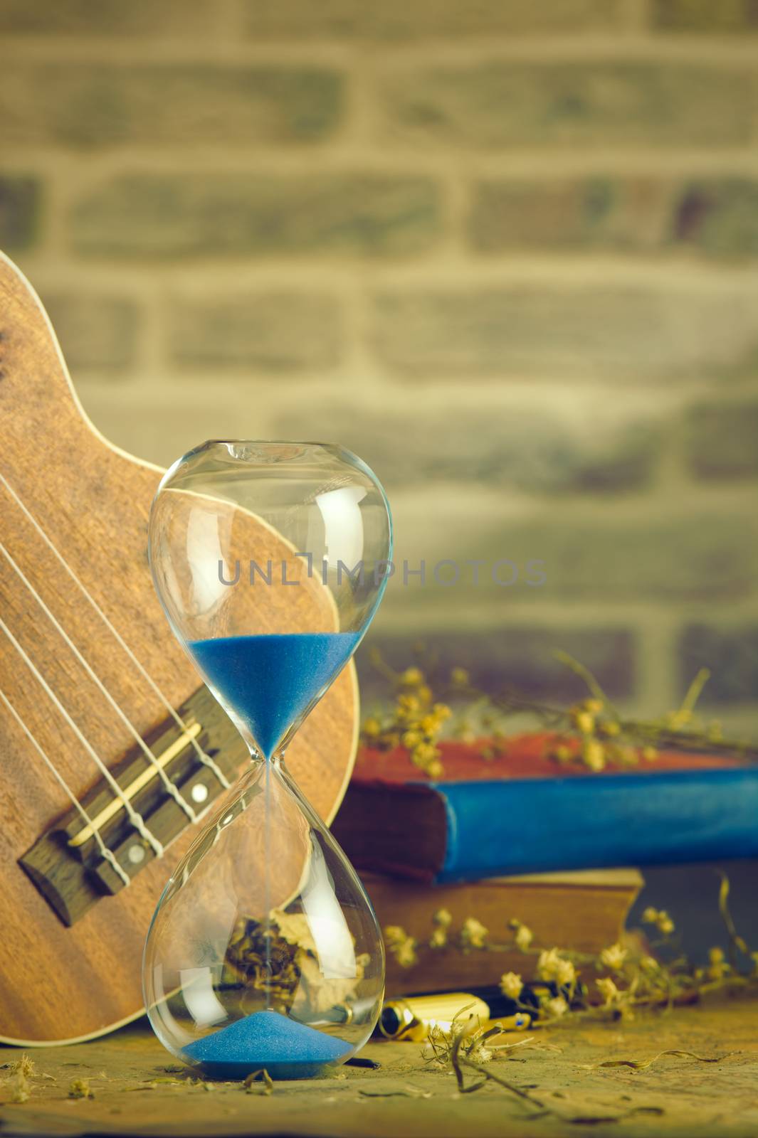 Hourglass and ukulele with an old book and brass pen on table. by SaitanSainam