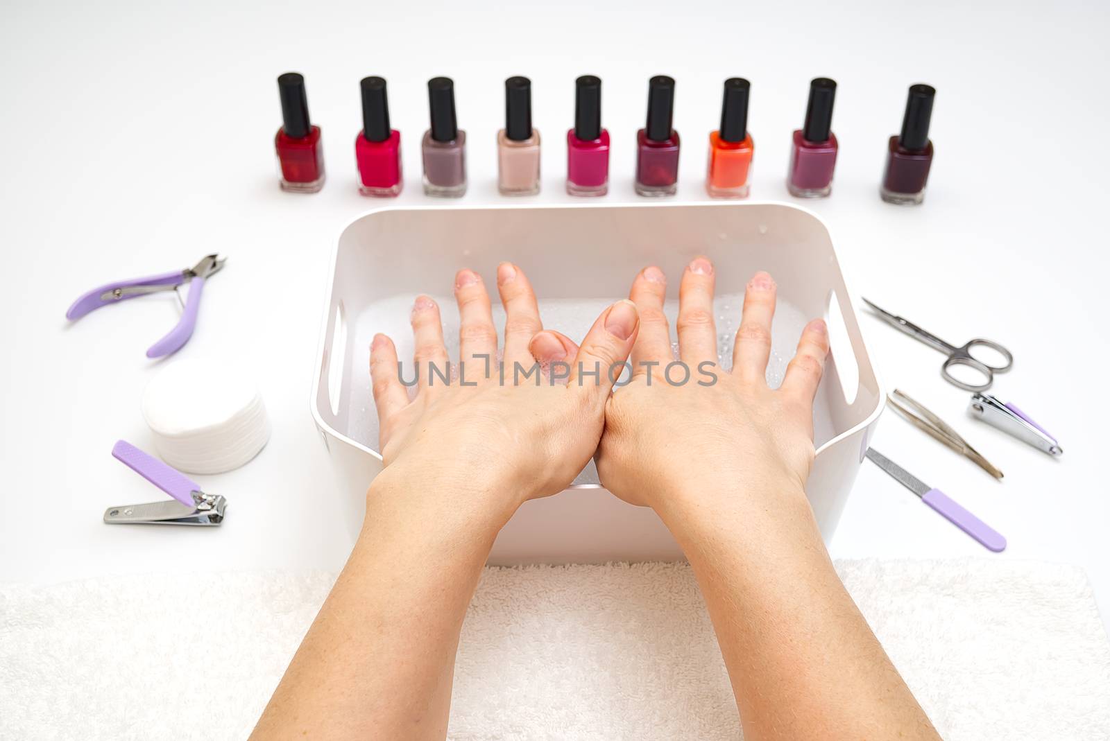 Manicure. Closeup of a woman hand polishing nails manicure. Nail technician manicure at nail salon. Young caucasian woman receiving a french manicure. by PhotoTime