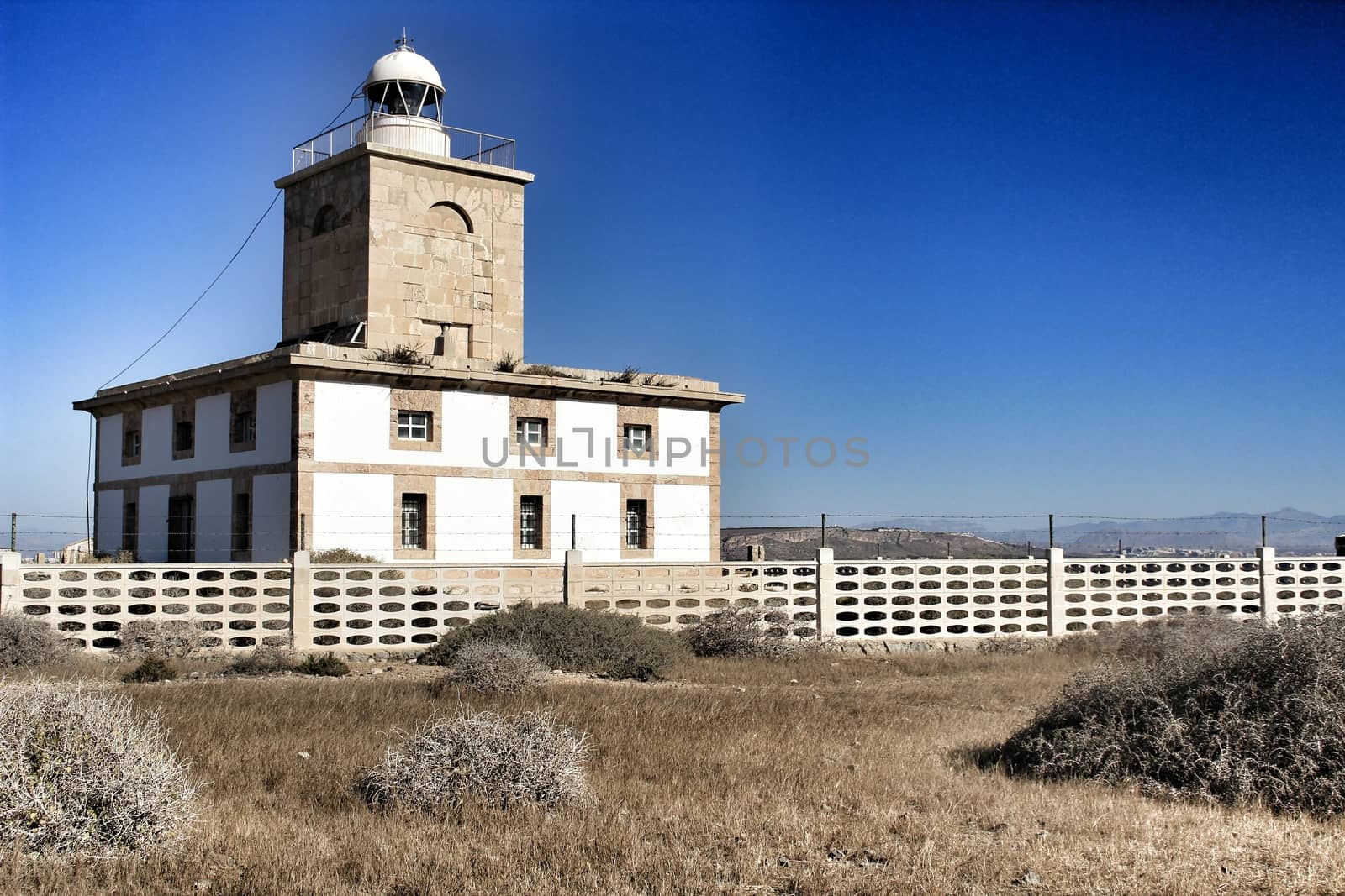 Lighthouse of Tabarca Island, Spain, surrounded by vegetation under blue sky in summer