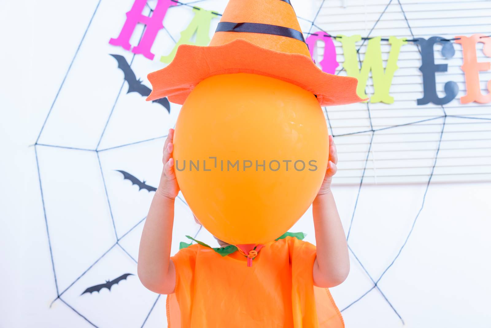 Funny happy kid boy in Halloween costume with Jack and have orange balloon on hand with Cobweb on background