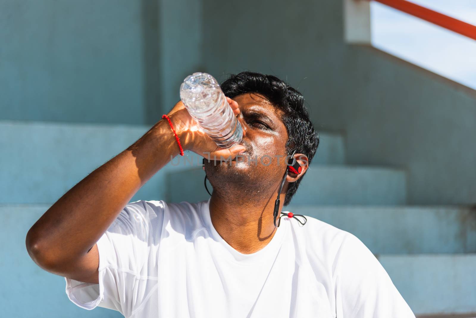 Close up Asian young sport runner black man wear athlete headphones he drinking water from a bottle after running at the outdoor street health park, healthy exercise workout concept