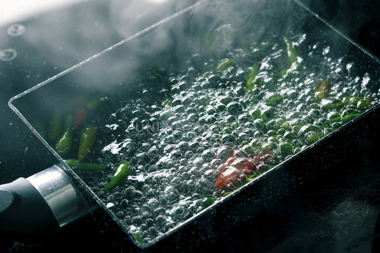 boiling water with chili pepper in pan on electric stove in kitchen, hot water with bubbles and steam