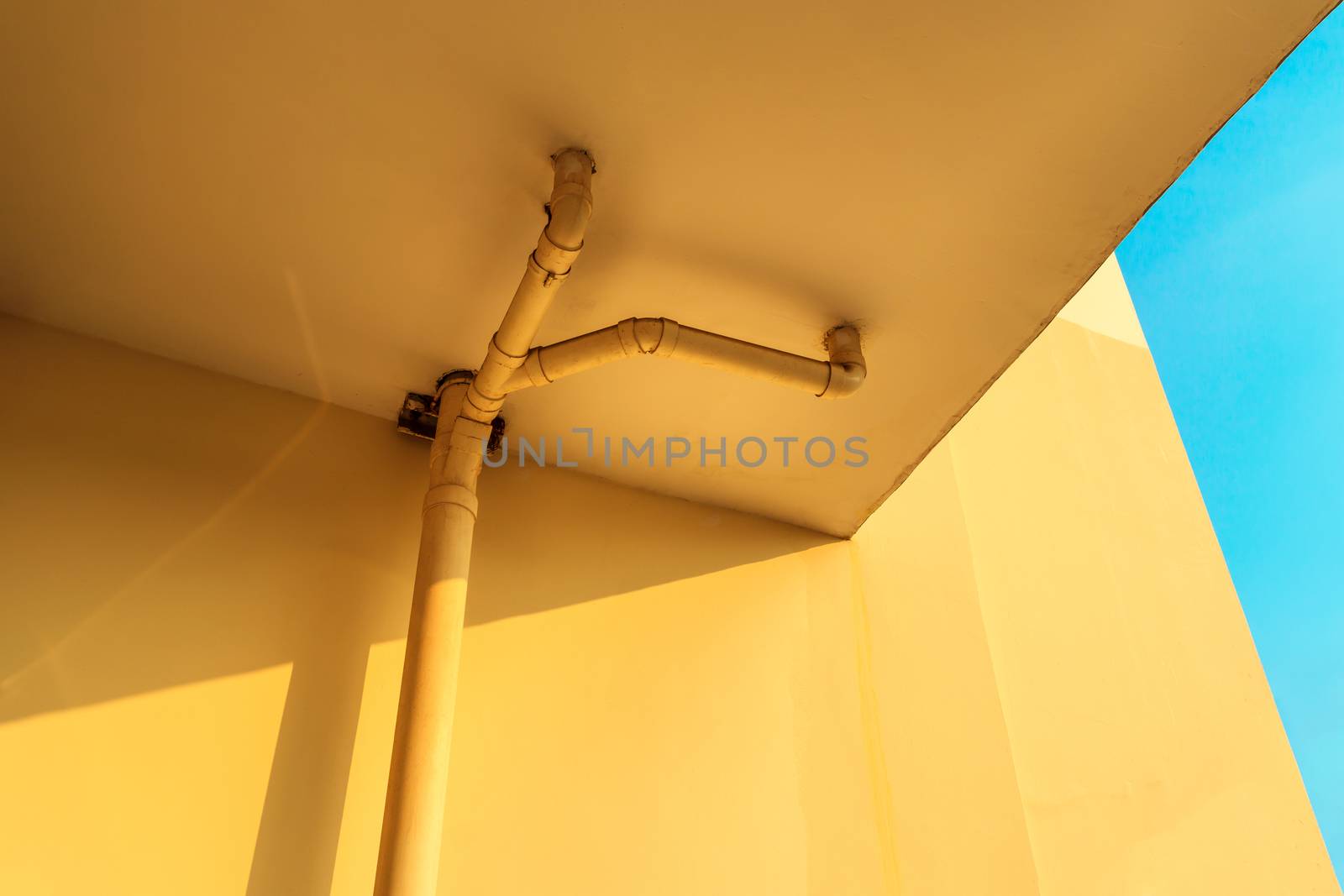 sewer pipes or drain pipes on yellow building wall with beautiful blue sky
