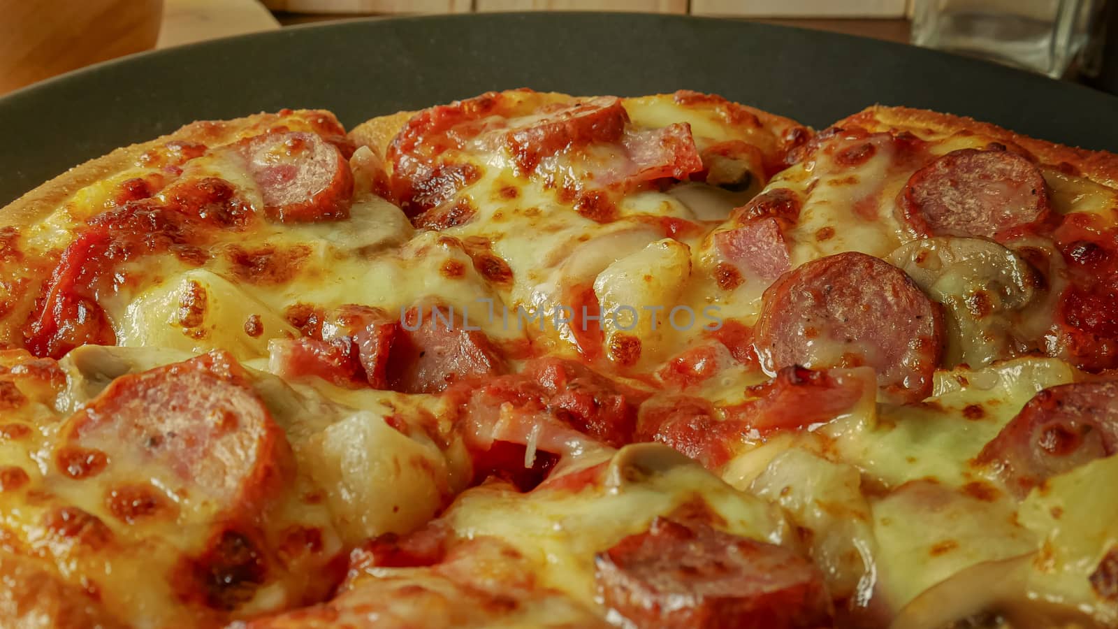 The pizza in black plate on wood table for food content.
