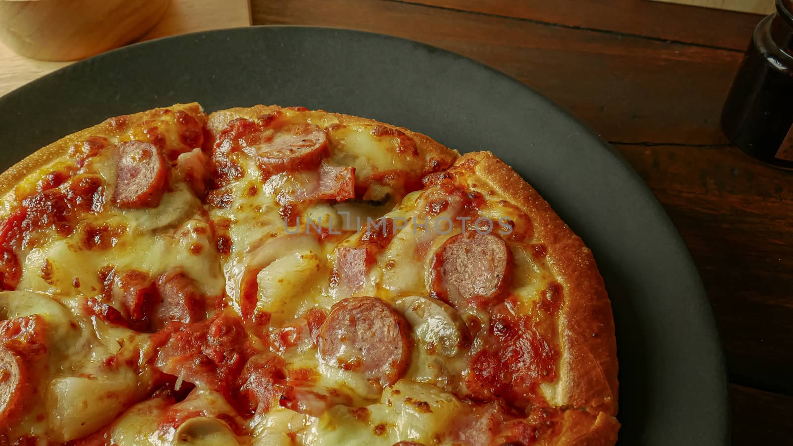 The pizza in black plate on wood table for food content.
