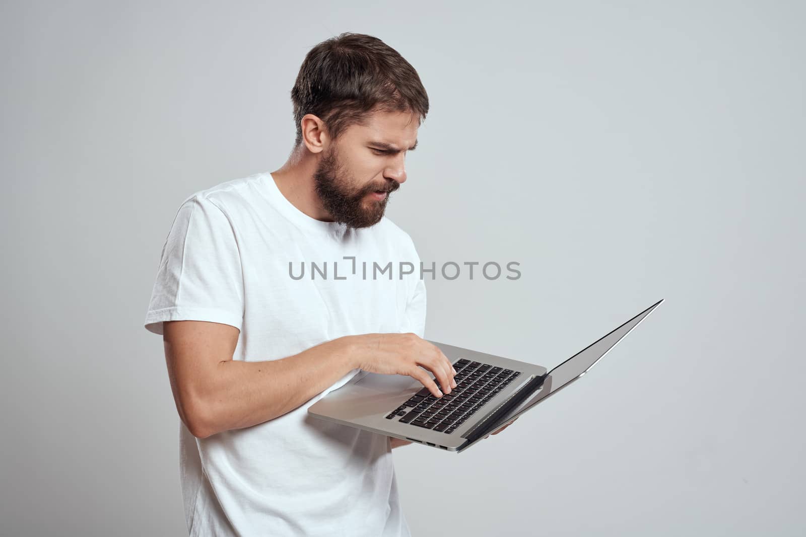 A man with a laptop in his hands on a light background in a white t-shirt emotions light background cropped view model portrait new technologies. High quality photo