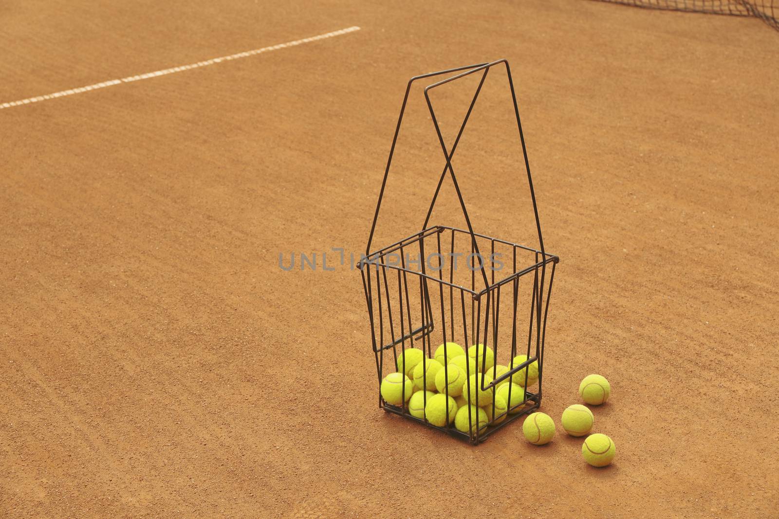 Basket with tennis balls on clay court, space for text