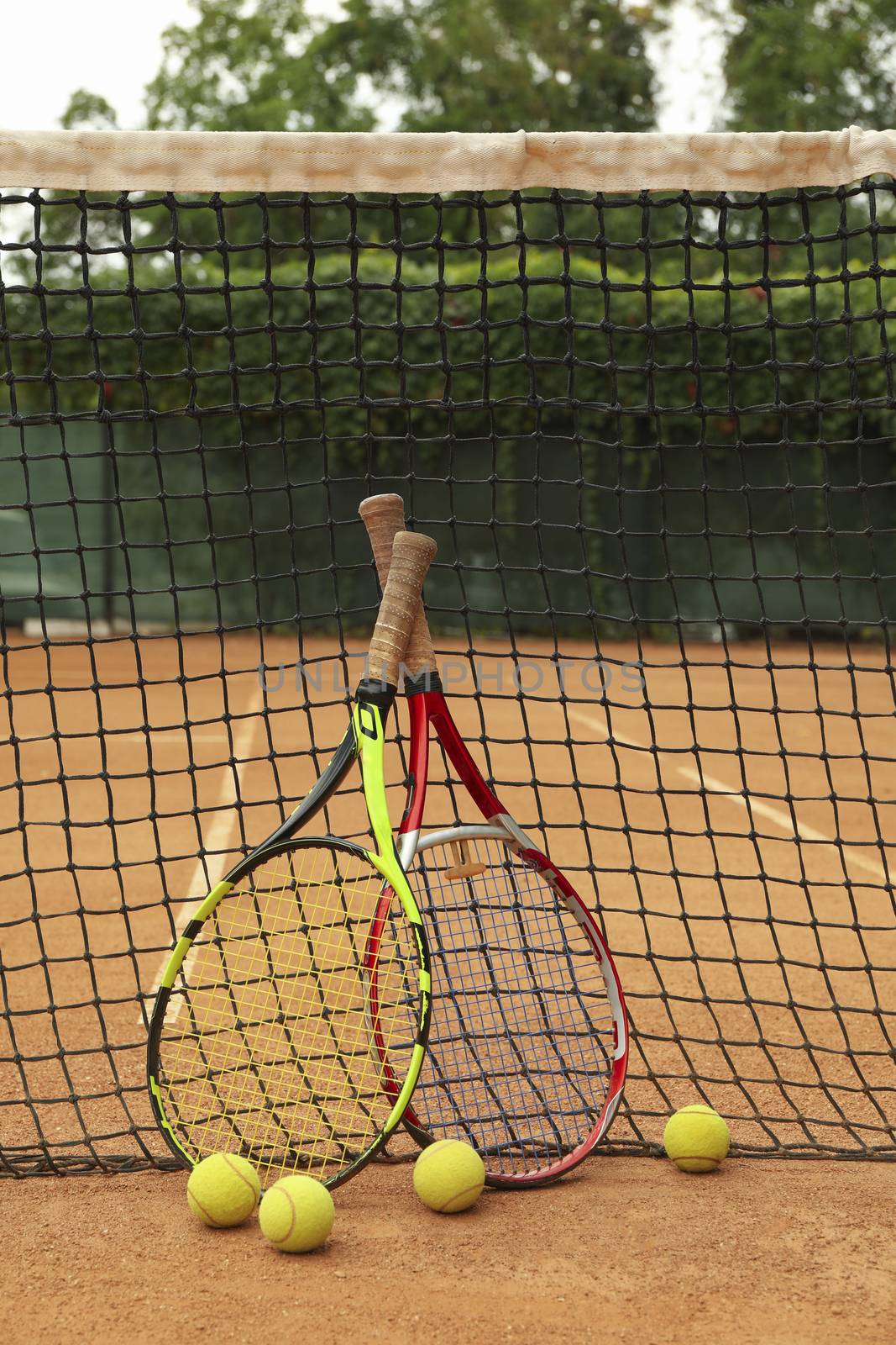Rackets and tennis balls against net on clay court