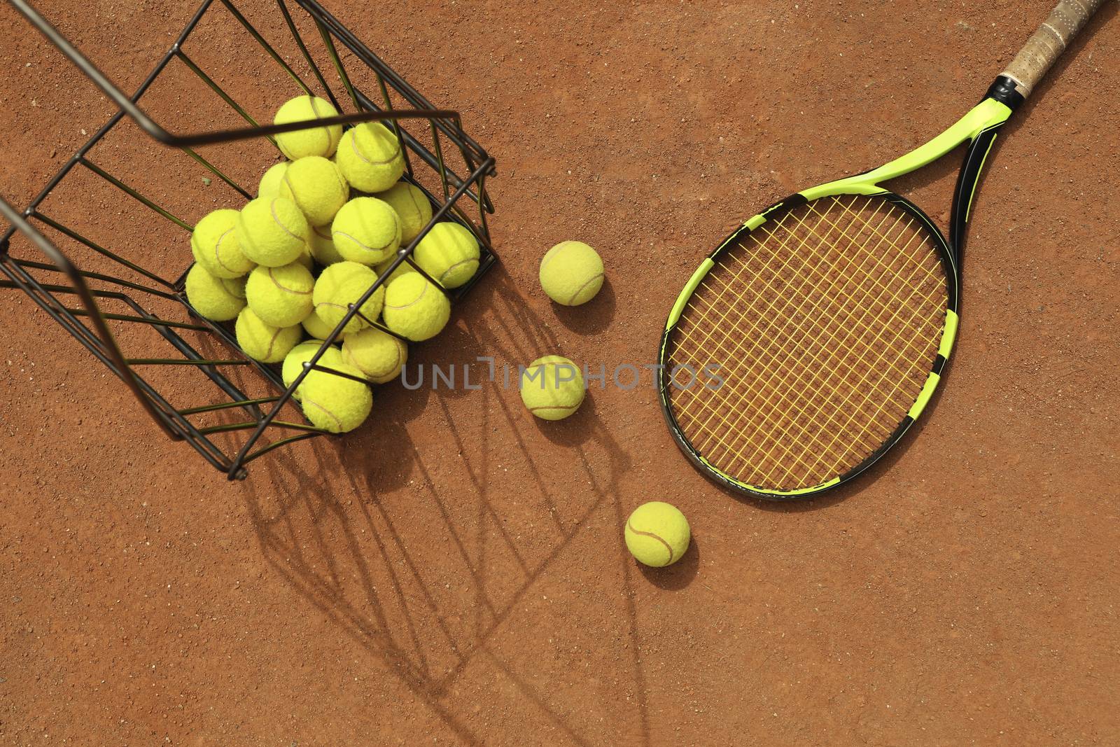 Racket and basket with tennis balls on clay court