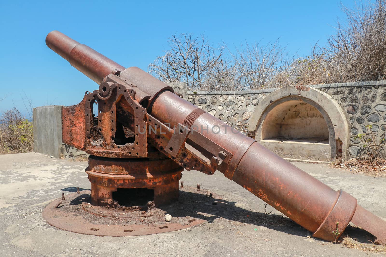 Old rusted cannon from World War II. Japanese cannon Meriam Jepang in a stone fortification on the island of Lombok in Indonesia. Color image of an old cannon on a sunny day by Sanatana2008