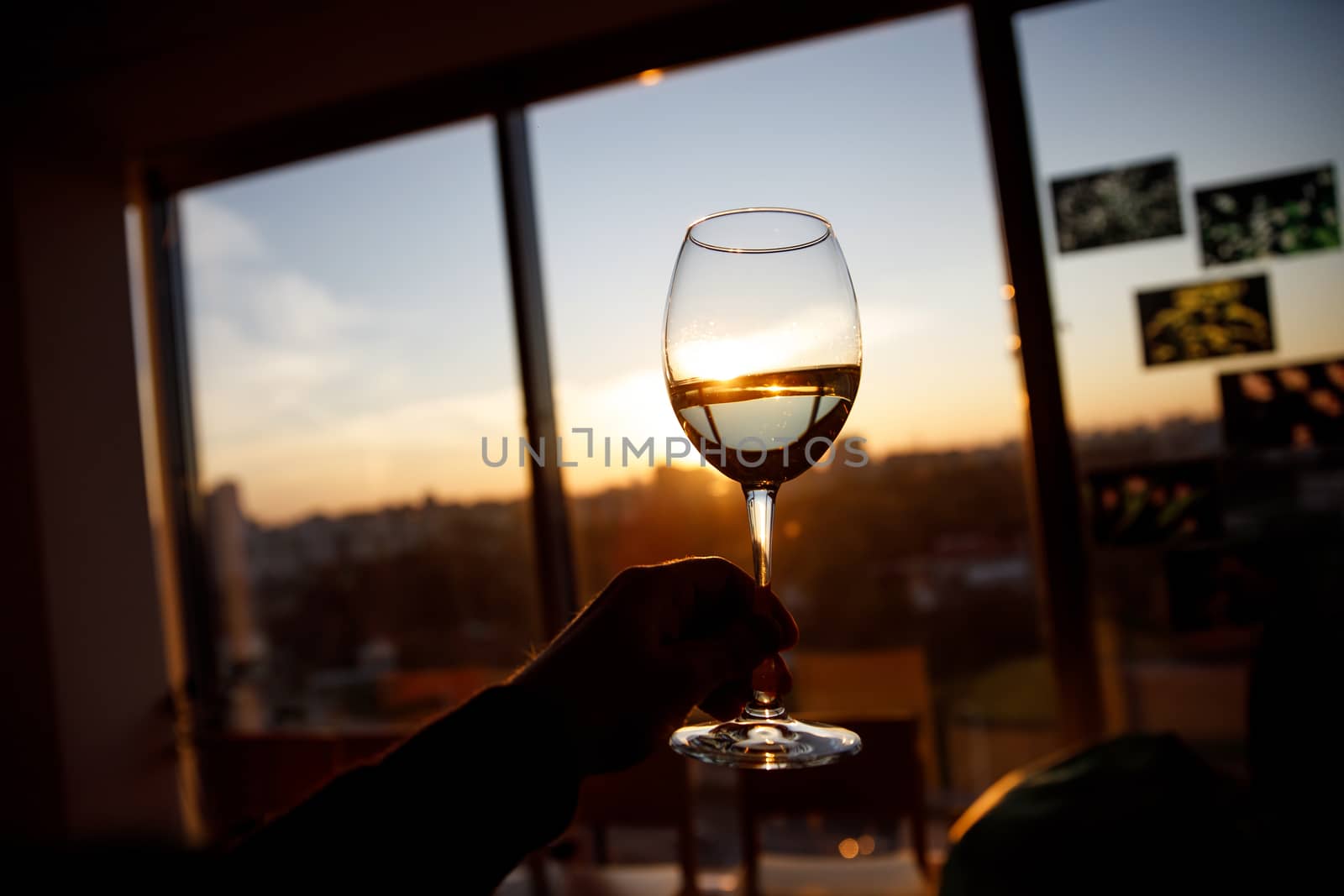 Wine glass in a hand over sunset. by 9parusnikov