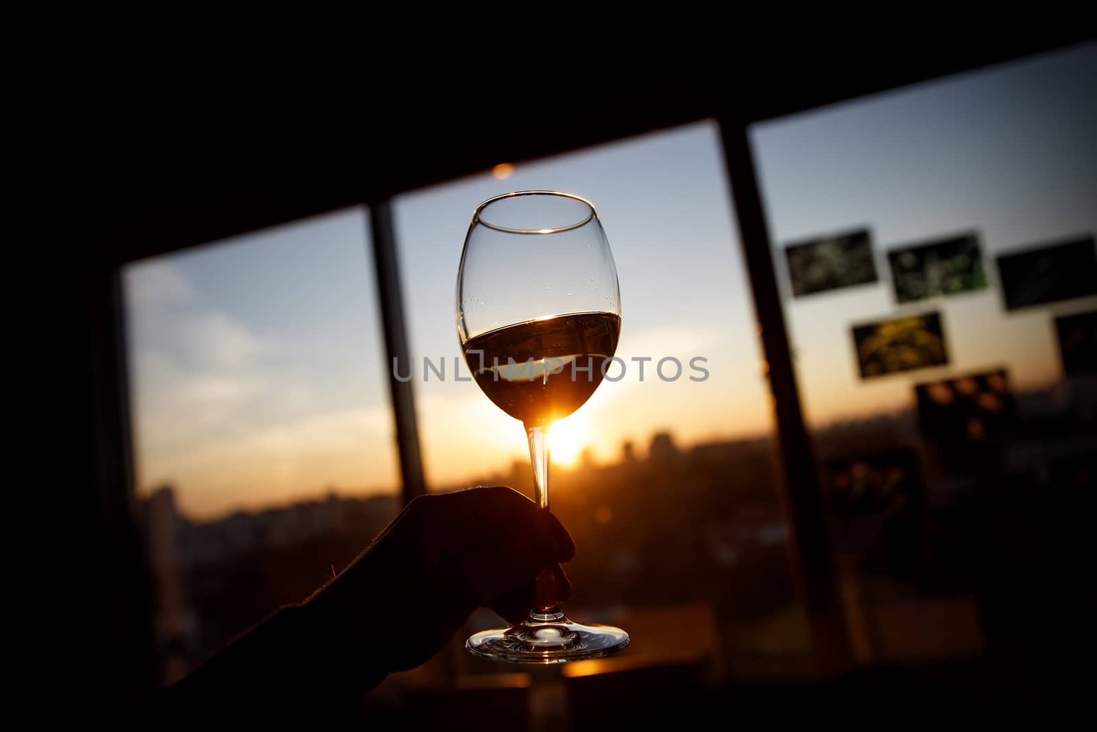 Wine glass in a hand over sunset. by 9parusnikov