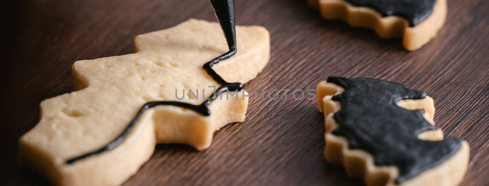 Close up of decorating cute Halloween bat gingerbread cookies with frosting icing cream topping bag.