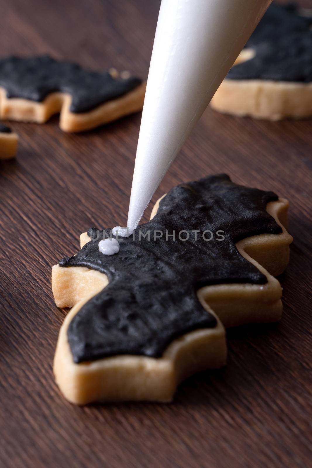 Close up of decorating cute Halloween bat gingerbread cookies with frosting icing cream topping bag.