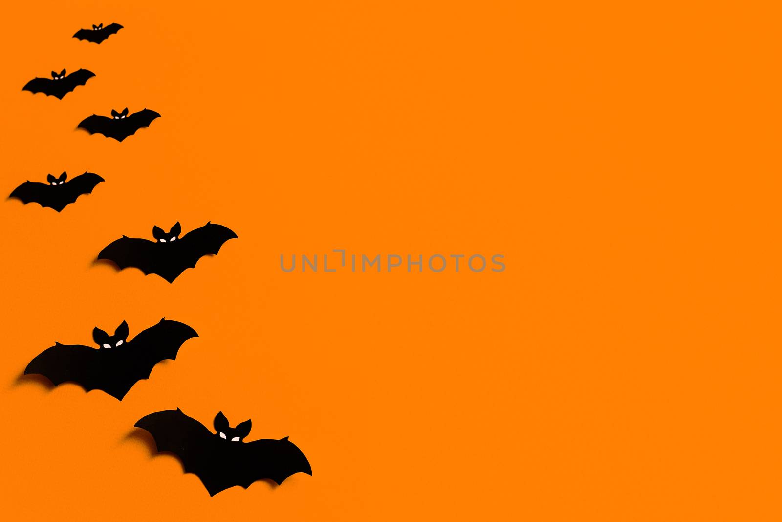 orange background with a flock of black paper bats for Halloween, black paper bat silhouettes on an orange background, Halloween concept, copyspace, flatlay, top view, overhead by Pirlik