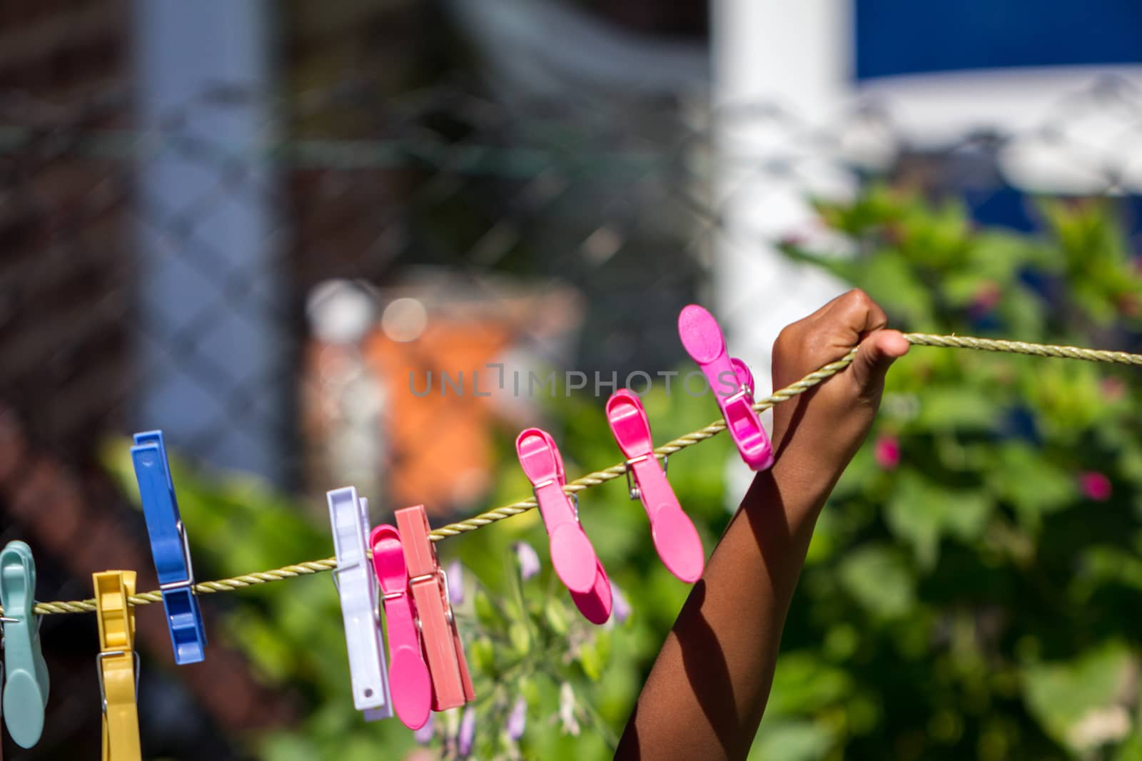 A young black child playing with clothes pegs and a washing line in the garden by magicbones