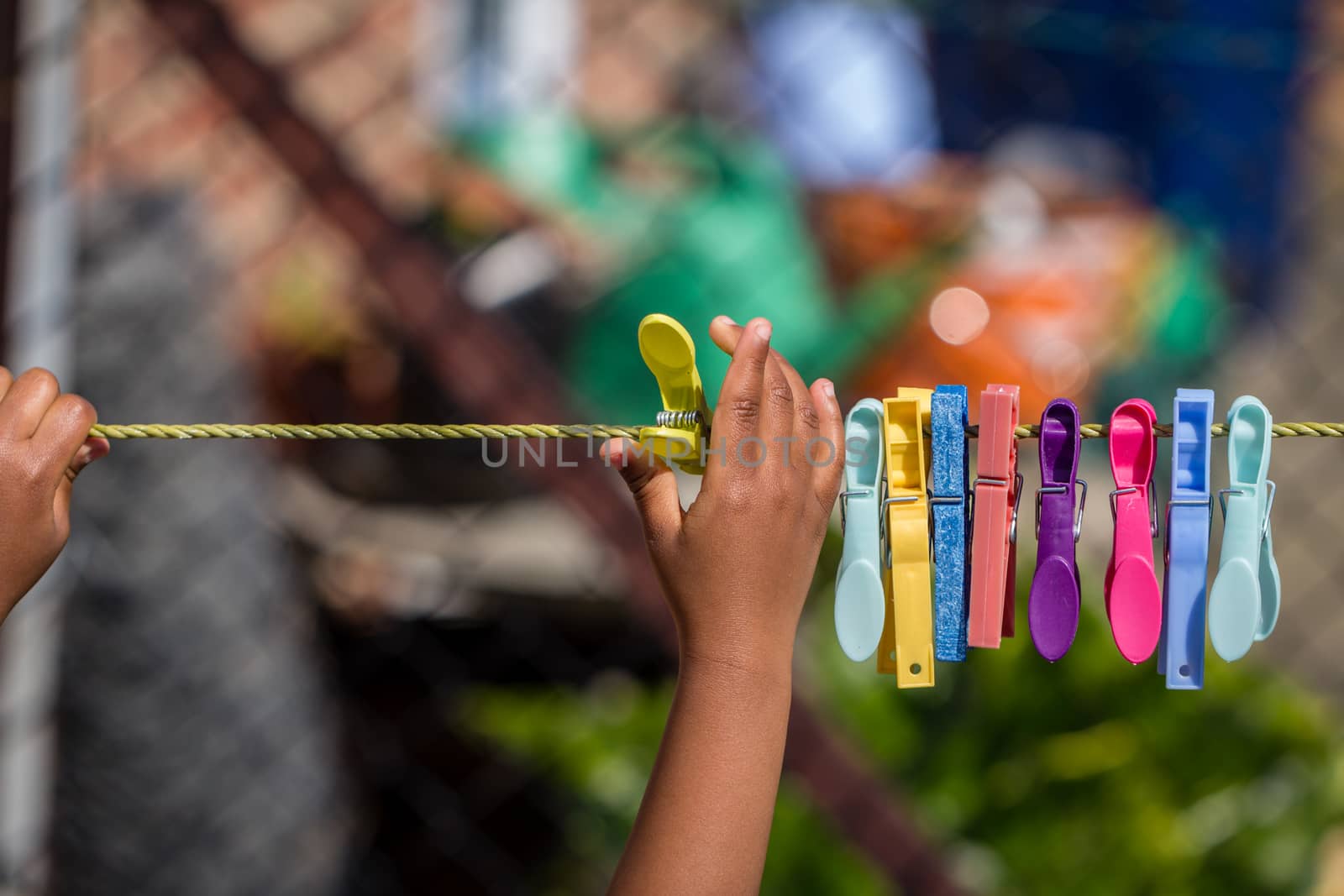 A young black child playing with clothes pegs and a washing line in the garden by magicbones