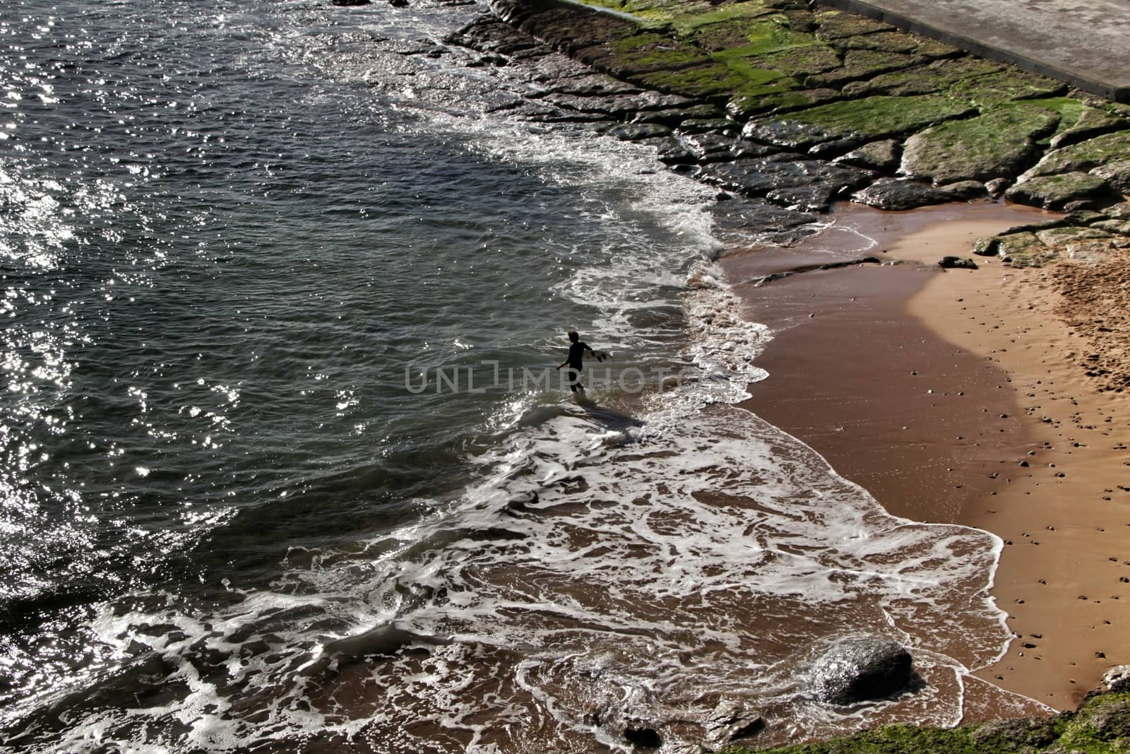 Surfer in the Beautiful Azarujinha beach with rock formations in Estoril, Lisbon, Portugal, in a sunny day of winter