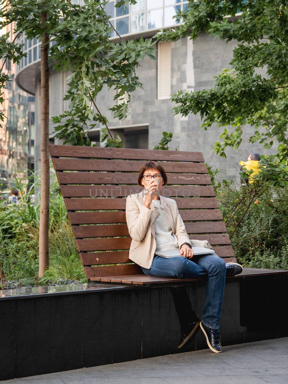 Freelance business woman sits in park with laptop and take away by aksenovko