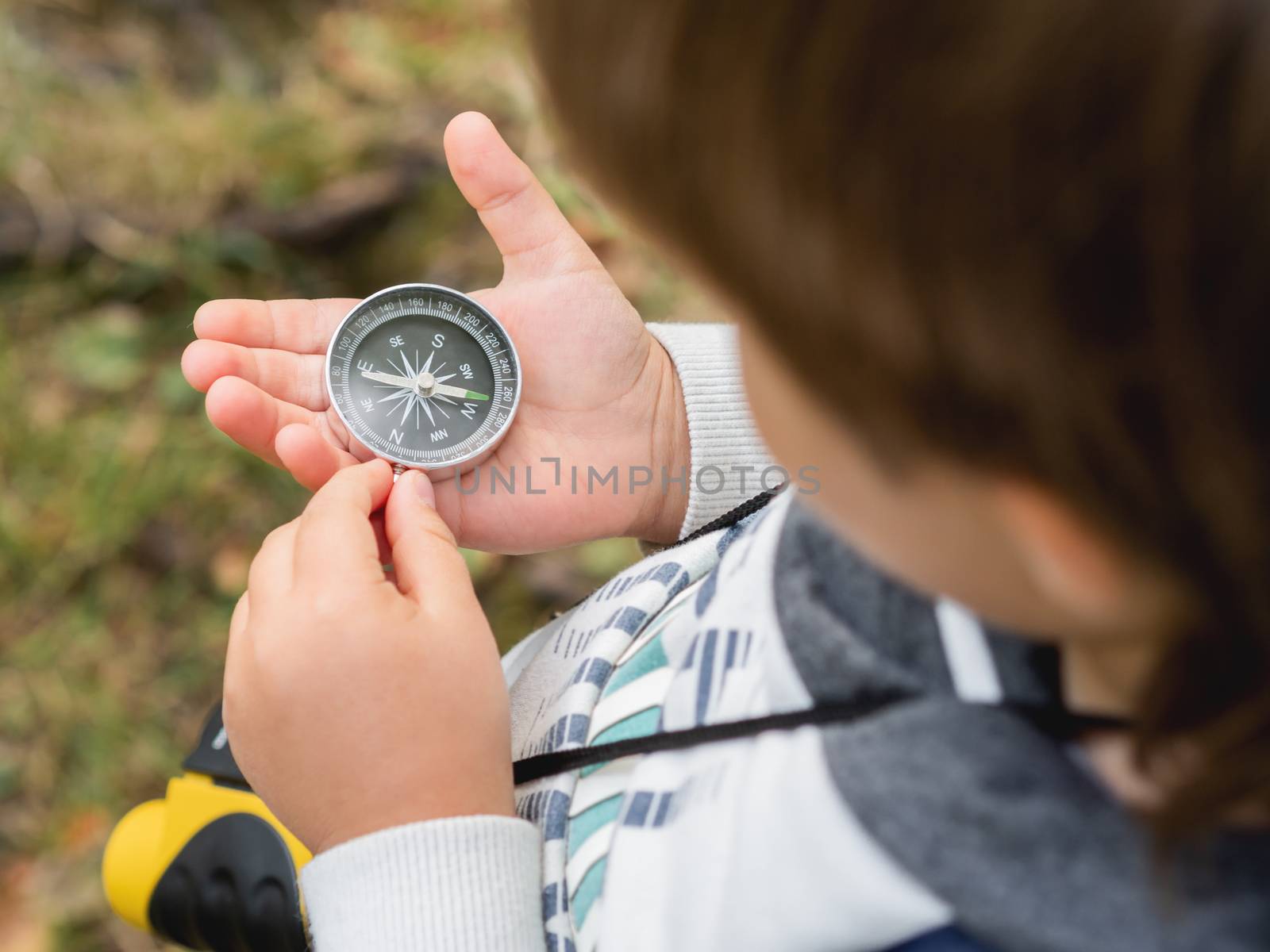 Little explorer on hike in forest. Boy with binoculars and compass sits on stump and reads map. Outdoor leisure activity for children. Summer journey for young tourist.