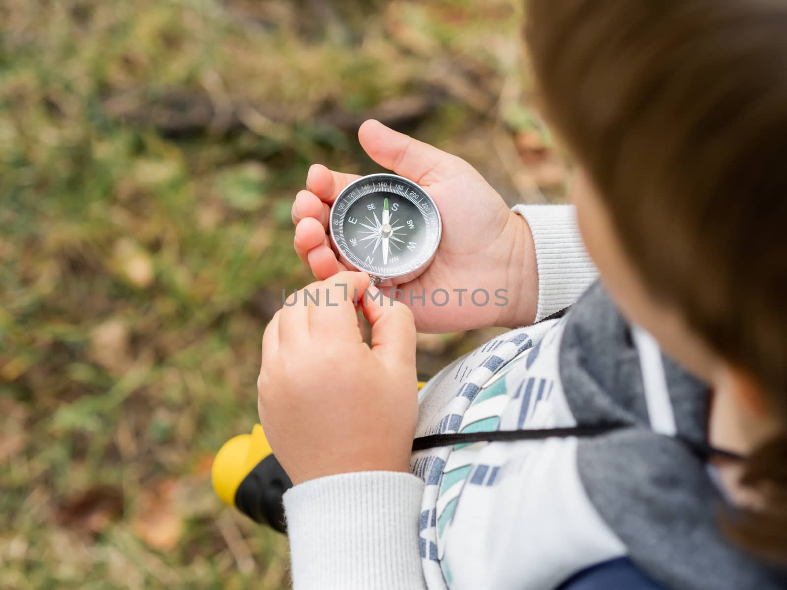 Little explorer on hike in forest. Boy with binoculars, backpack, water bottle and rope sits on stump and reads map. Outdoor leisure activity for children. Summer journey for young tourist.