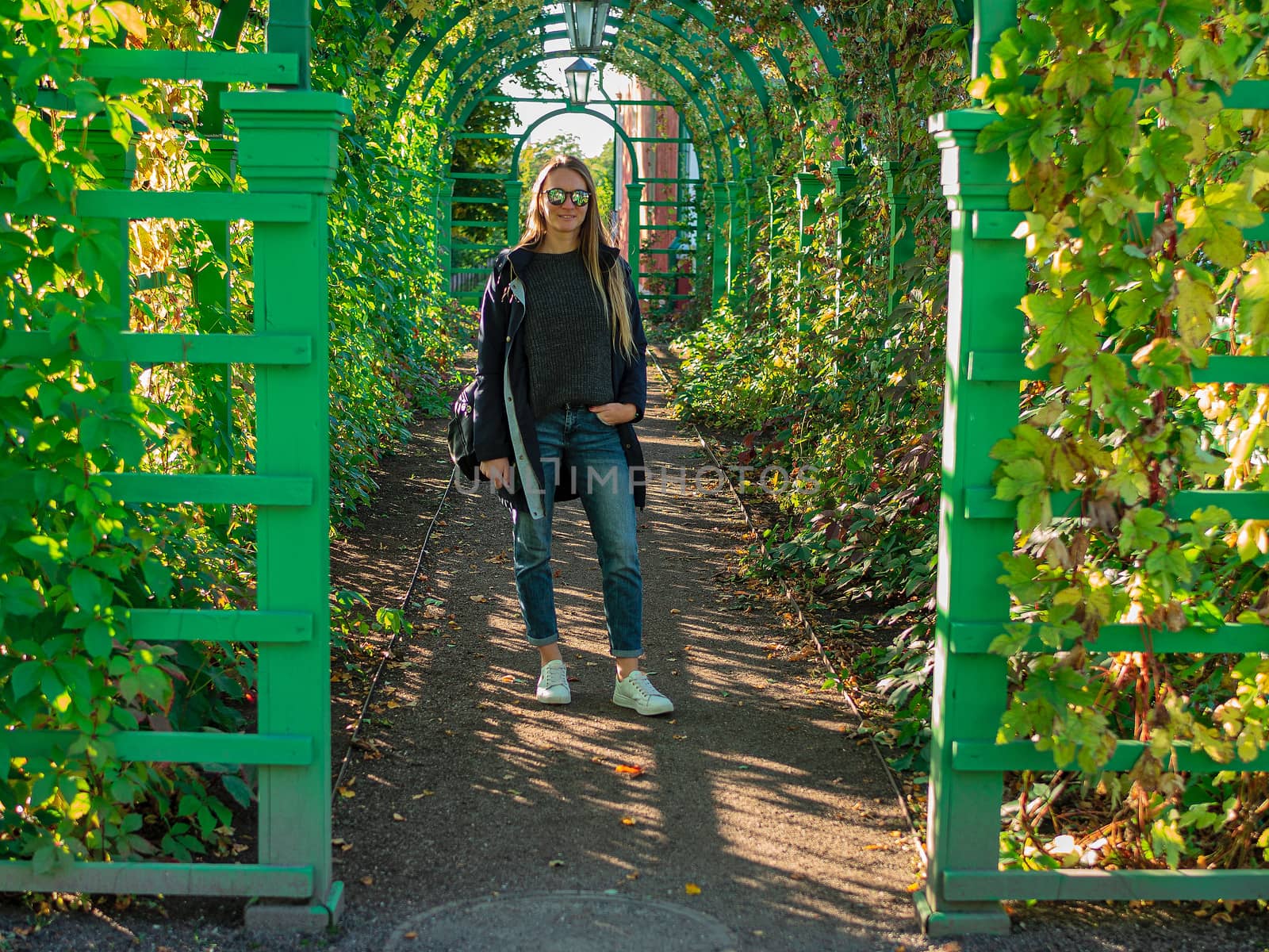 Photo of caucasian Pretty young girl while walking outdoor through field with flowers. Woman with long hair and dark coat in nature. autumn in Estonia. Green backgroun. Copy space