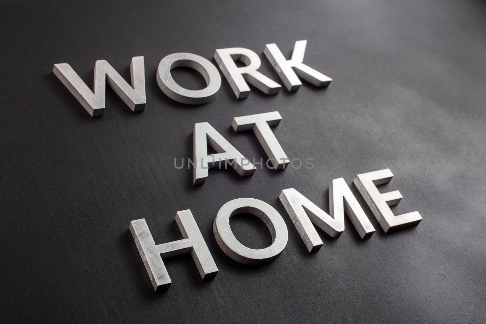 the words work at home laid with silver metal letters on matte black background in diagonal perspective, full frame view