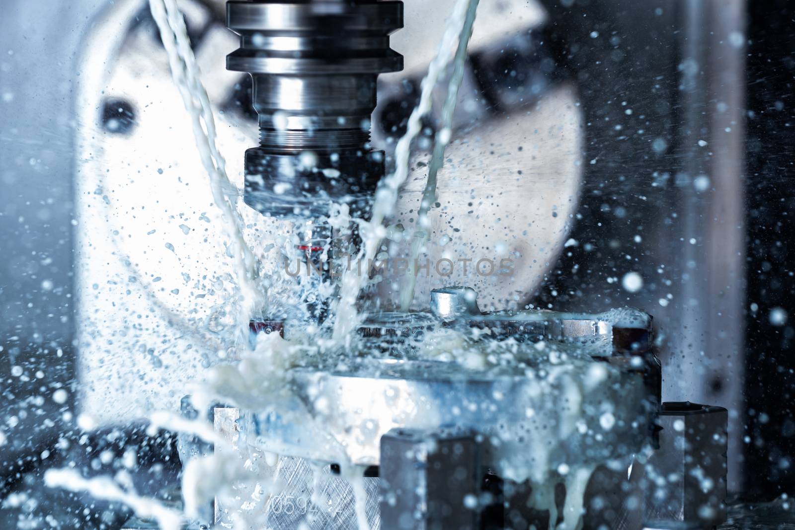 A process of vertical cnc steel milling with external water coolant streams and splashes. Fast shutter speed for motion freezing.