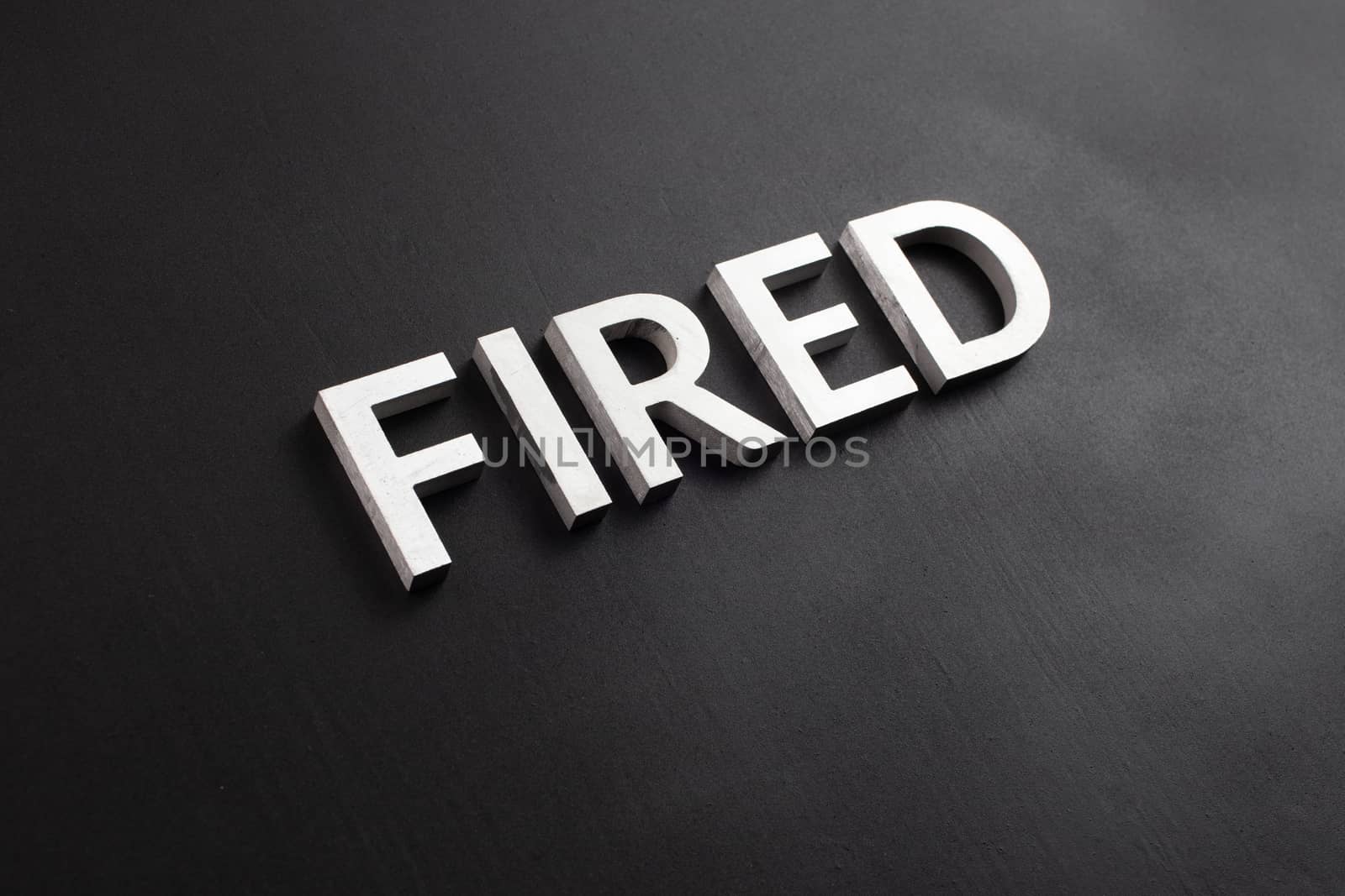 the word fired laid with white brushed metal letters on flat black surface in diagonal perspective with selective focus and background blur