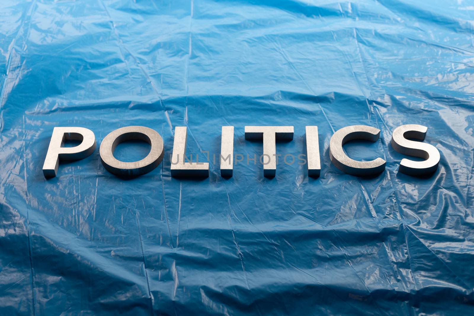 the word politics laid with silver aluminium letters over crumpled plastic blue film background - in center of picture.