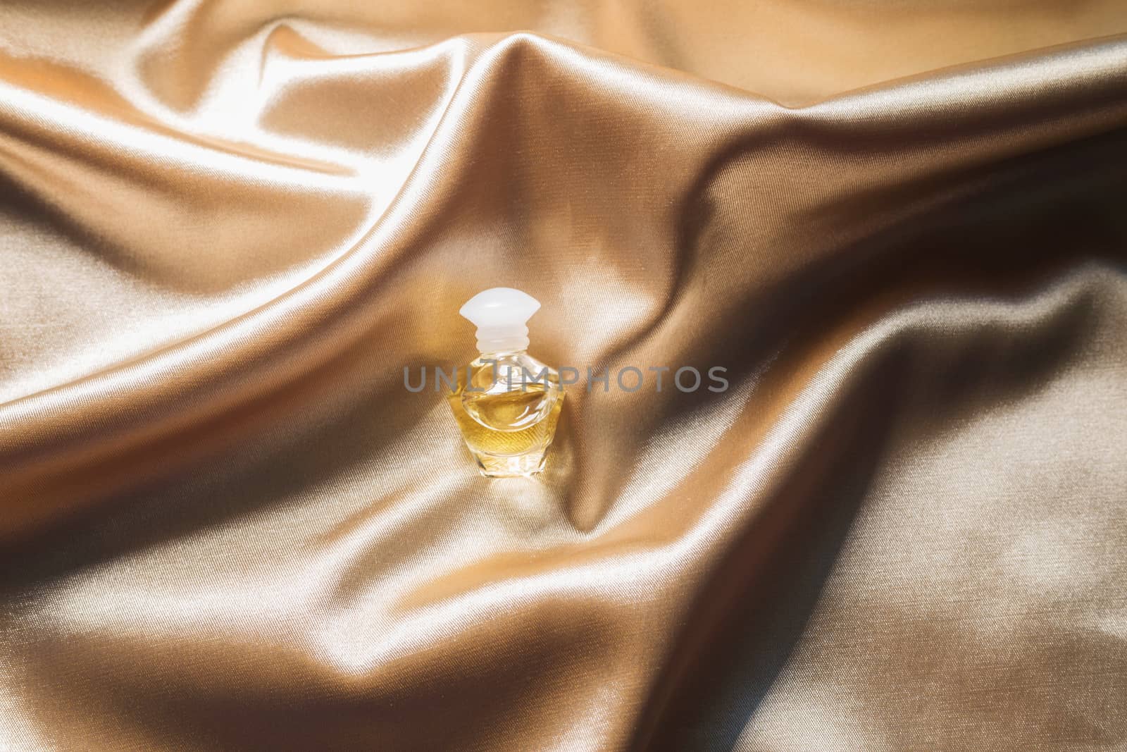 .Perfume bottle on gold folded silk fabric background. Luxery Scent fragrance cosmetic beauty product.