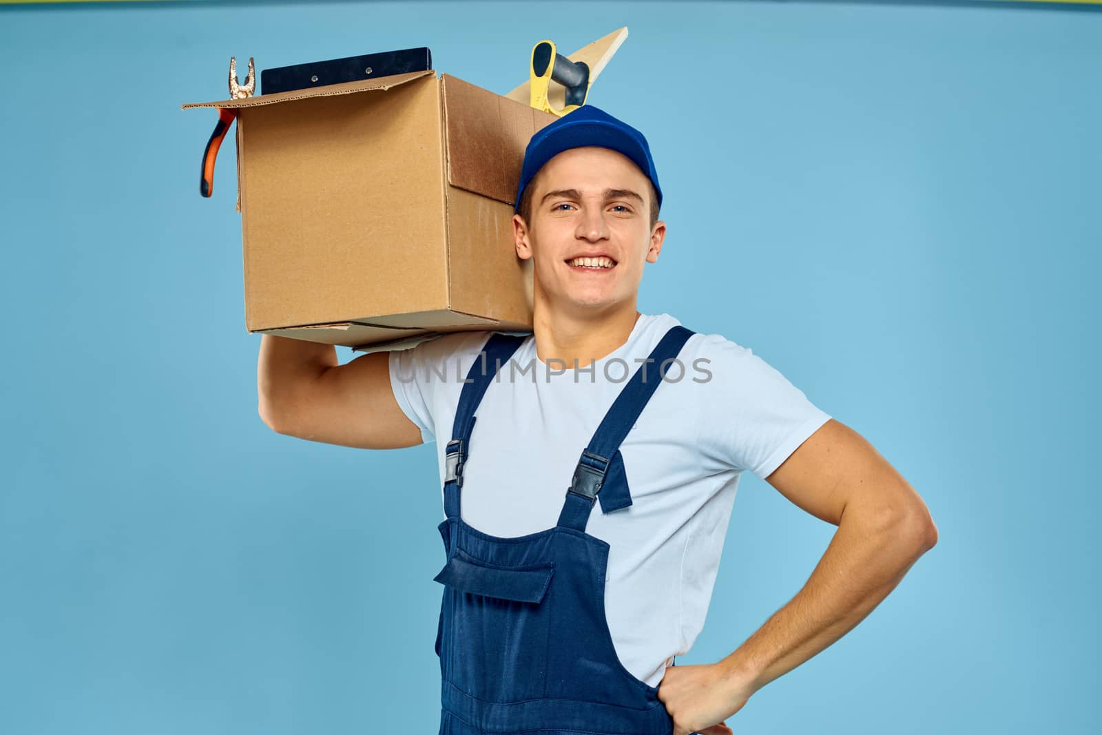 working man in uniform box with tools loader delivery blue background by SHOTPRIME