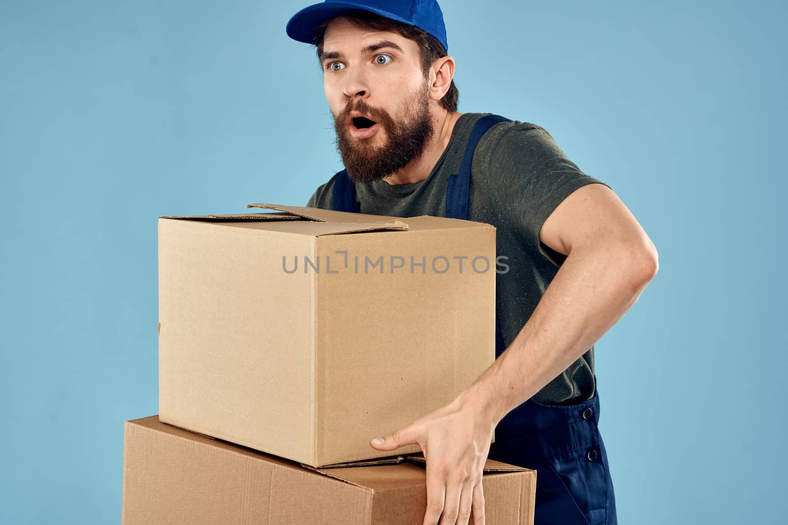 Man in working uniform with boxes in hands delivery service blue background by SHOTPRIME