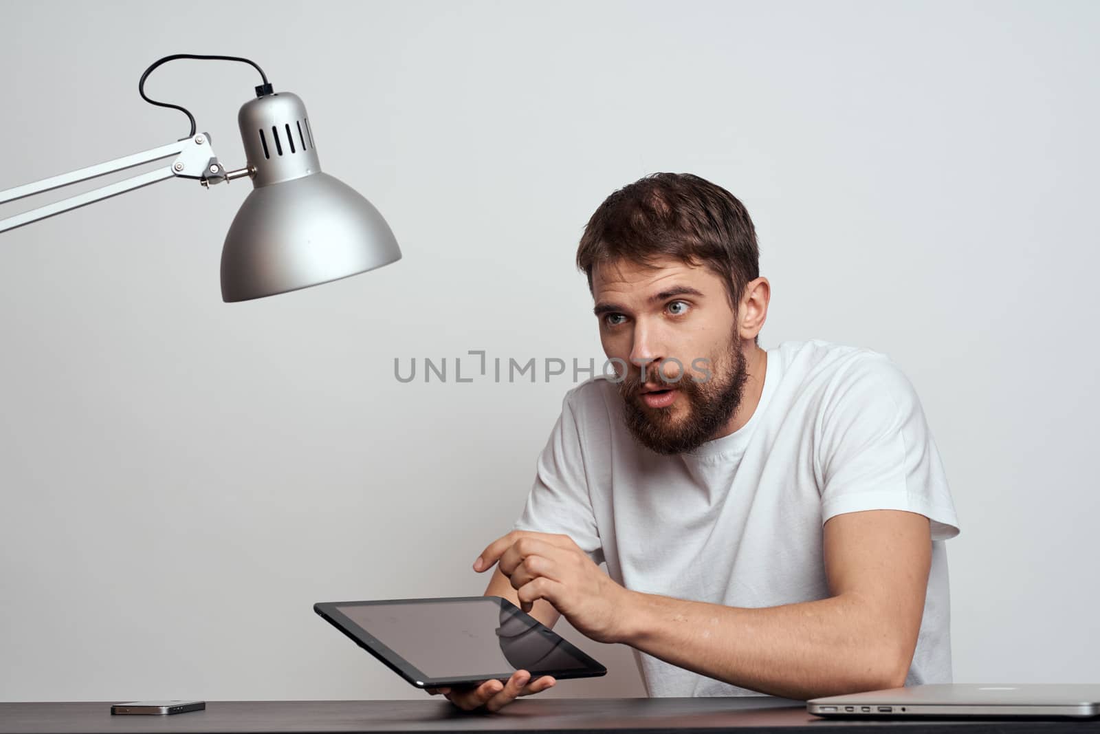 A man with a tablet at the table gestures with his hands on a light background and an iron lamp. High quality photo