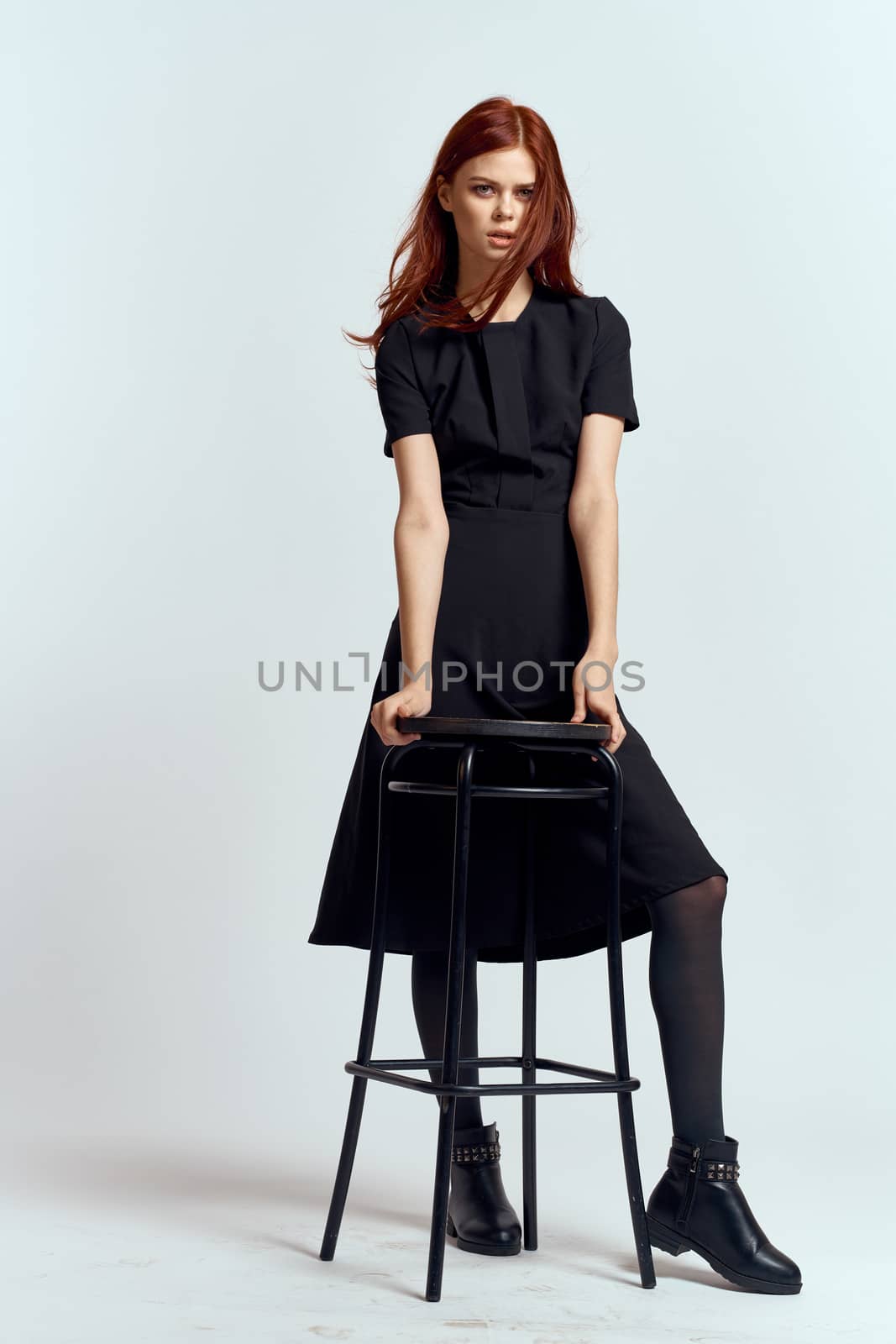woman high chair indoors full length black dress red hair model boots. High quality photo