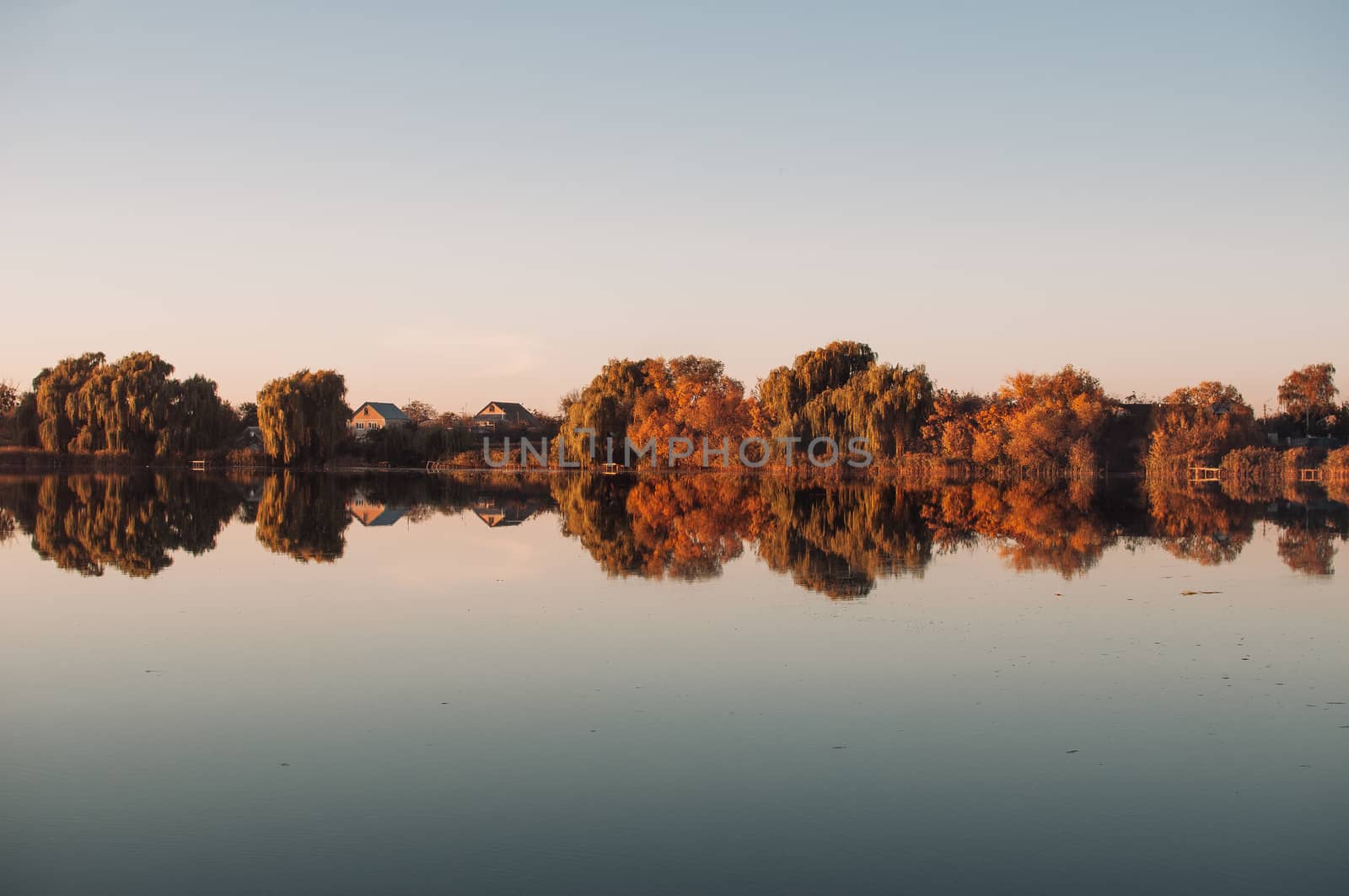 Orange sunset against the background of the river in September in the harvest season. Reflection in the water from the trees. Beautiful autumn landscape. Autumn colors are reflected in calm waters.