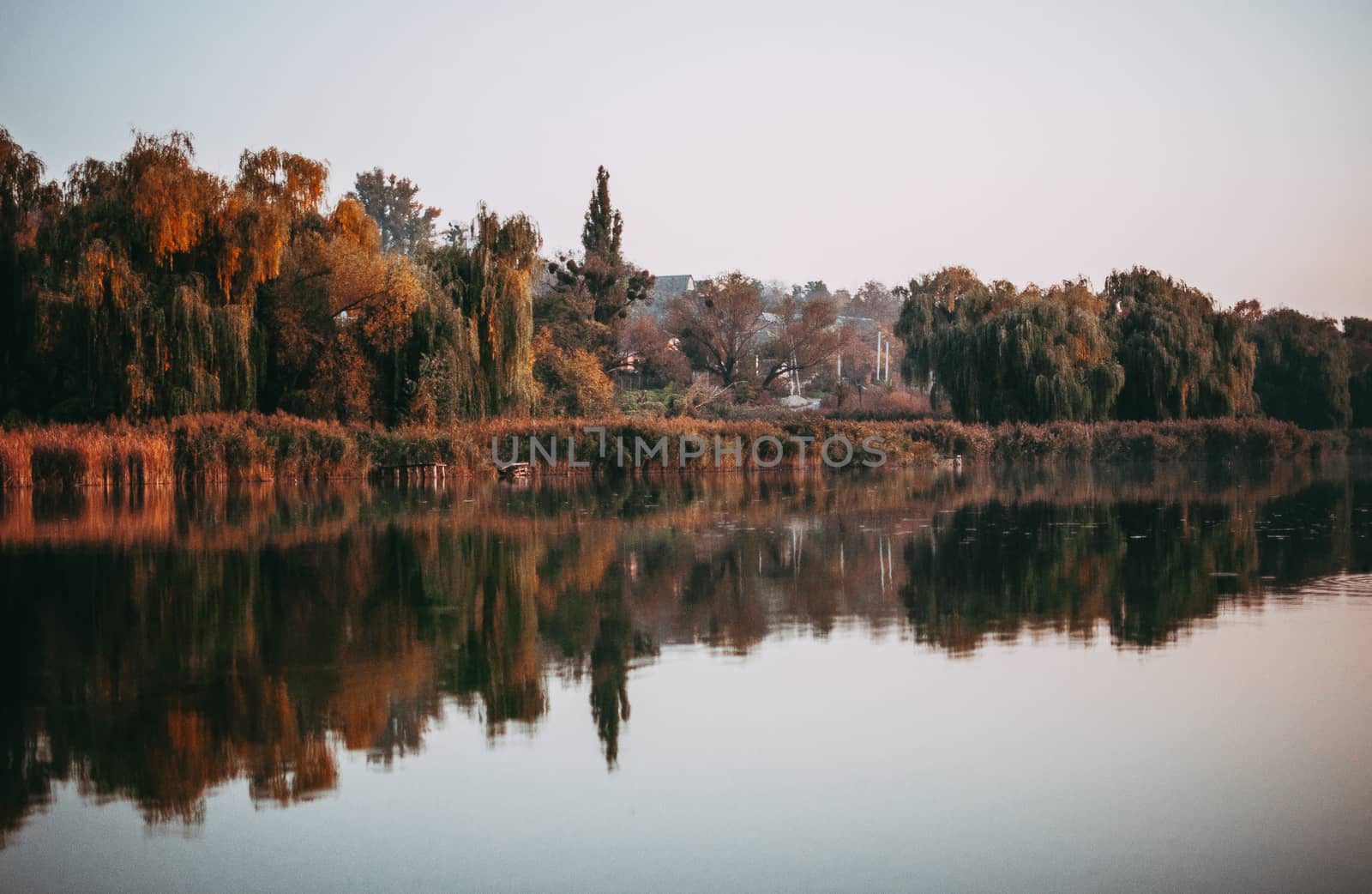 sunset against the background of the river in September in the harvest season. Reflection in the water from the trees. Beautiful autumn landscape. Autumn colors are reflected in calm waters.