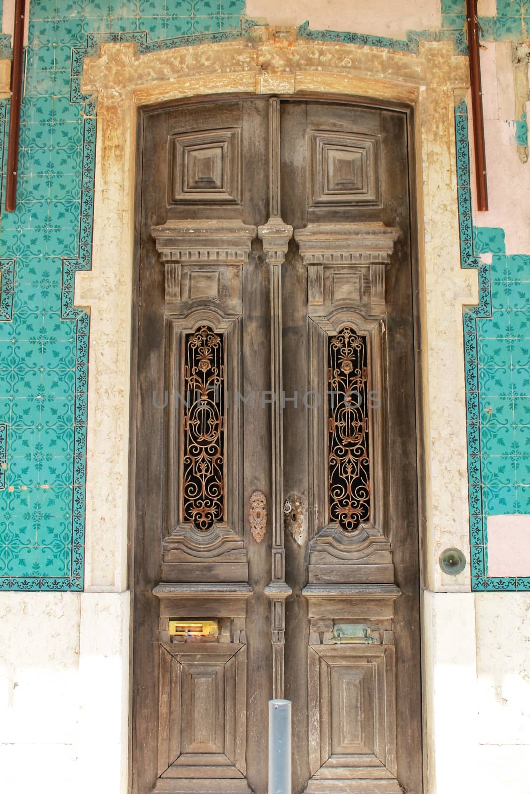 Old wooden door with tiled facade in Lisbon. Wrought metal details on the door.