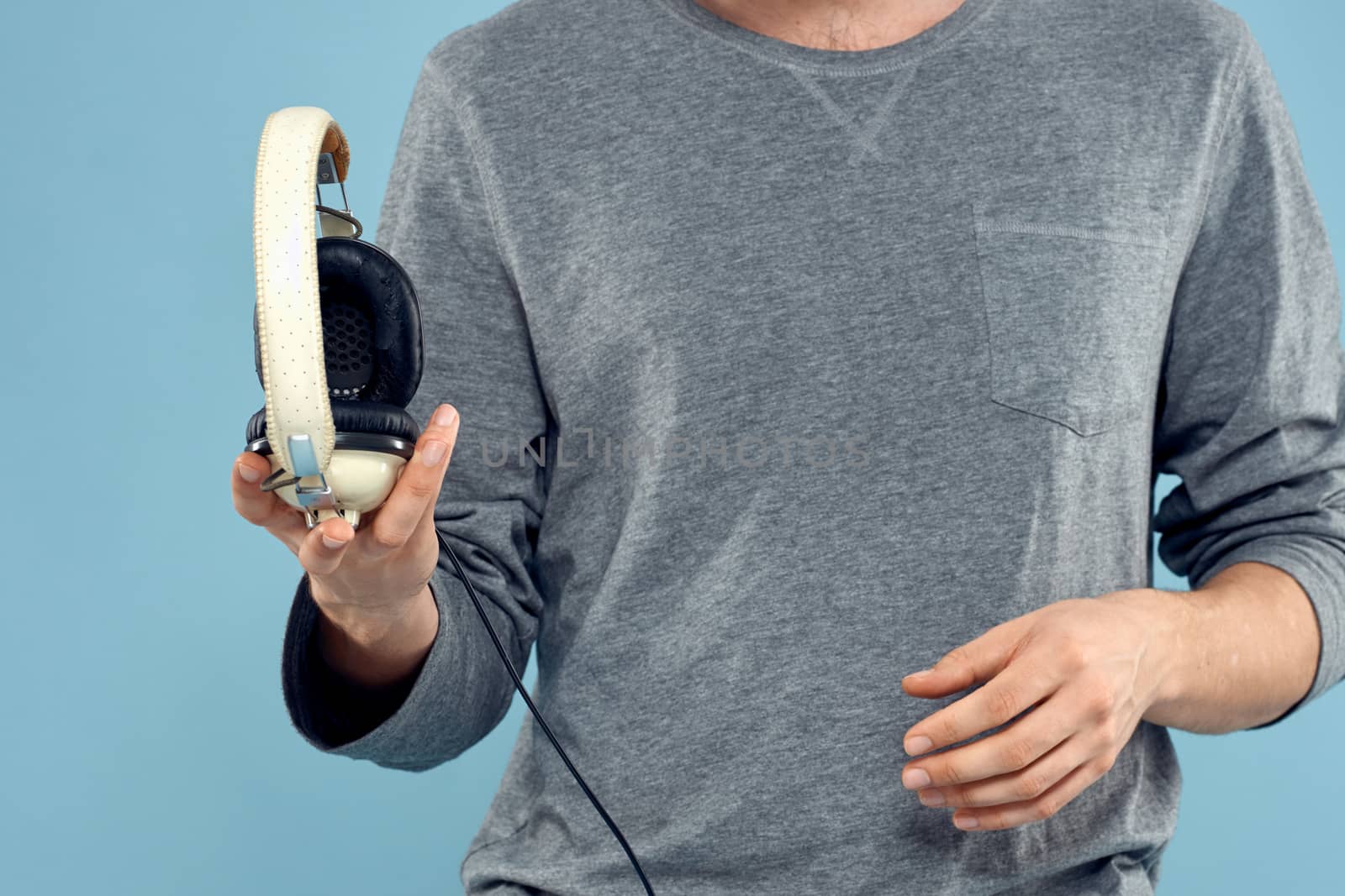 Headphones in man hands cropped view music technology blue background by SHOTPRIME