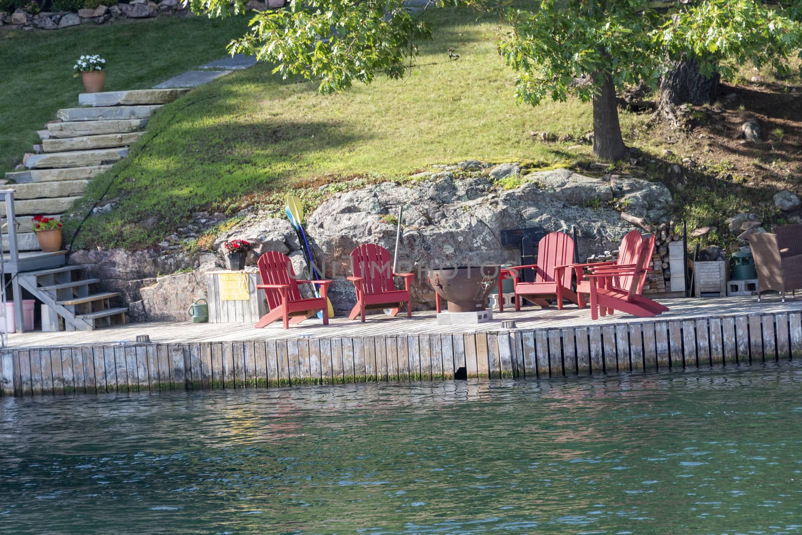 Chairs are arranged and a barbecue is set on the rocks and prepared for a picnic on a wooden pier