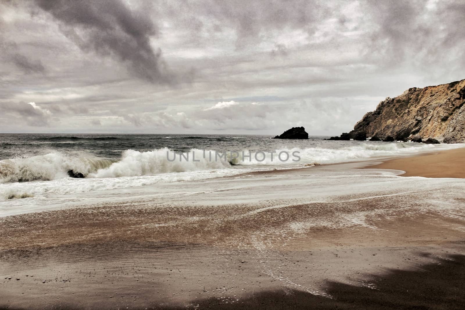 Brave ocean, rock formations and cloudy drama sky on the beach of Adraga in Sintra, Lisbon, Portugal