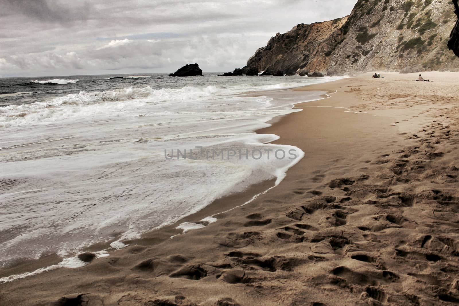 Brave ocean, rock formations and cloudy drama sky on the beach of Adraga in Sintra, Lisbon, Portugal