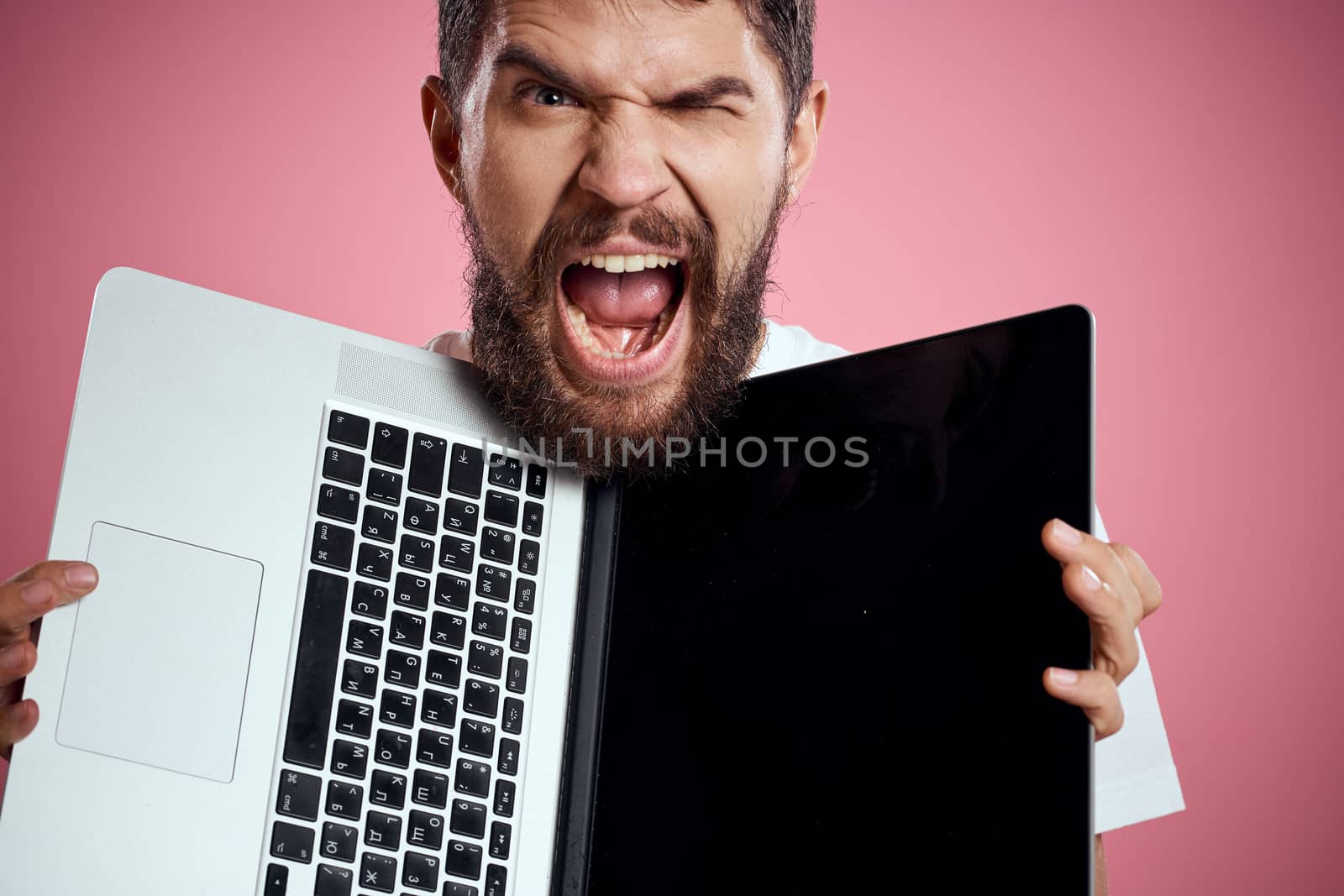 A man with an open laptop on a pink background white t-shirt gestures with his hands cropped view new technology keyboard monitor. High quality photo