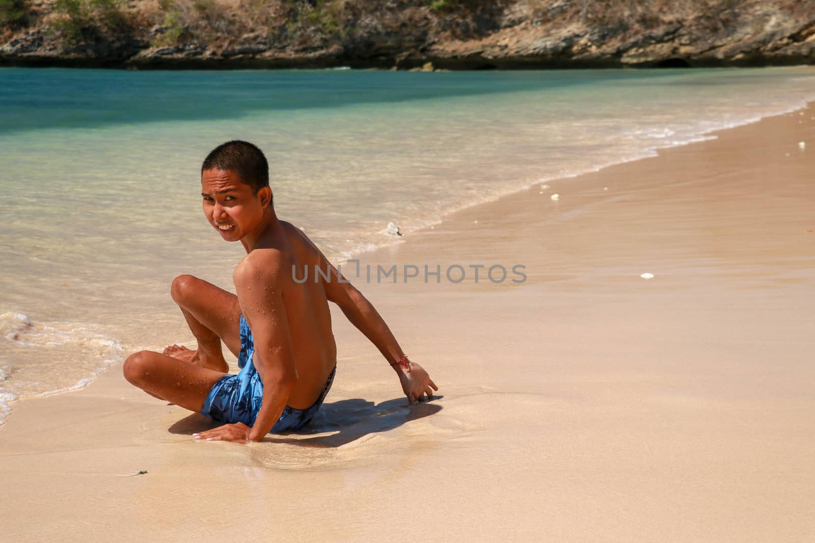 Portrait of an attractive young man on a tropical beach. Selective focus young man sit on the beach, copy space. Asian teenager sitting on a sandy beach and looking into the lens.