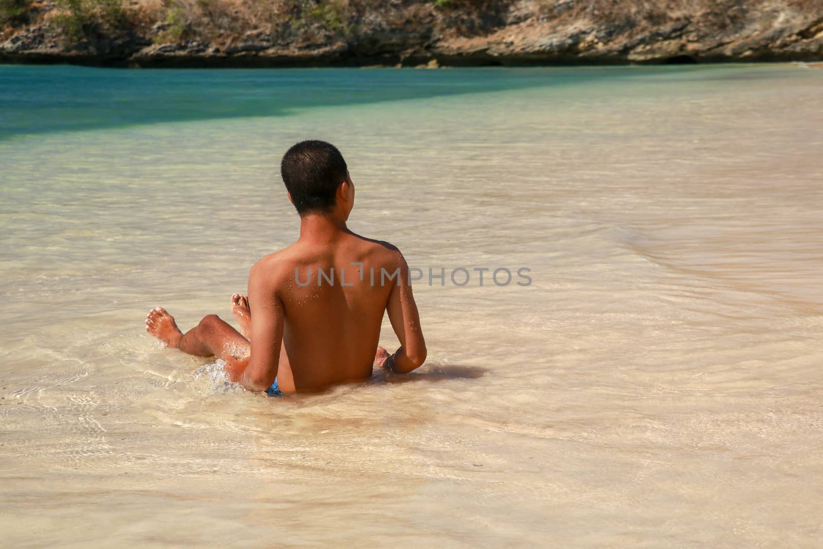 Rear view of a young man sitting on a sand beach. The blue sea and idyllic nature scene destination. Asian handsome teenager sitting and enjoying the view on the tropical beach by Sanatana2008
