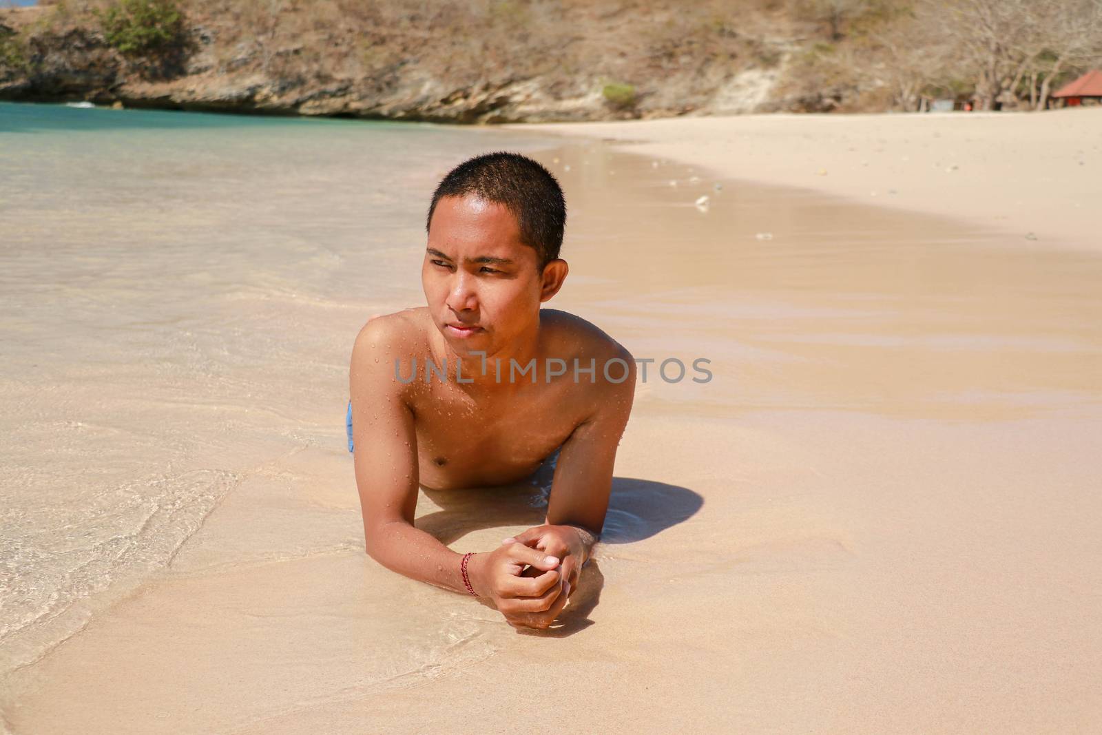 Sexy male model lying in the water on his stomach. Happy Asian man sunbathing on the beach on vacation.
