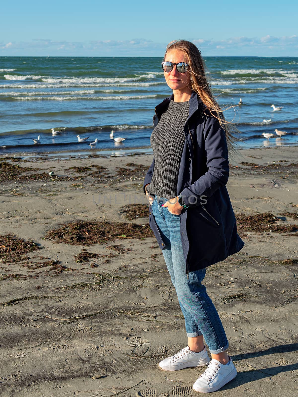 Pretty young girl ashore the Baltic sea. Young woman with long hair and dark coat in nature. autumn beach of the Baltic Sea. Blue sea on the backgroun. Copy space