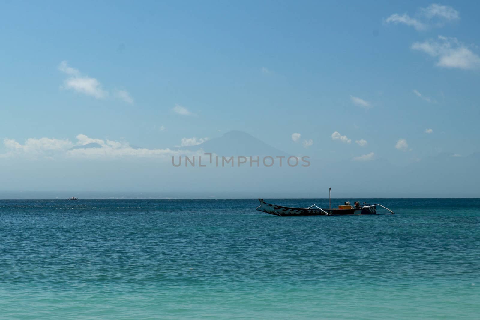 View of Rinjani volcano from Pink Beach Lombok. Bay with turquoise blue water and fishing boat anchored on calm sea level. Beach with its transparent water.