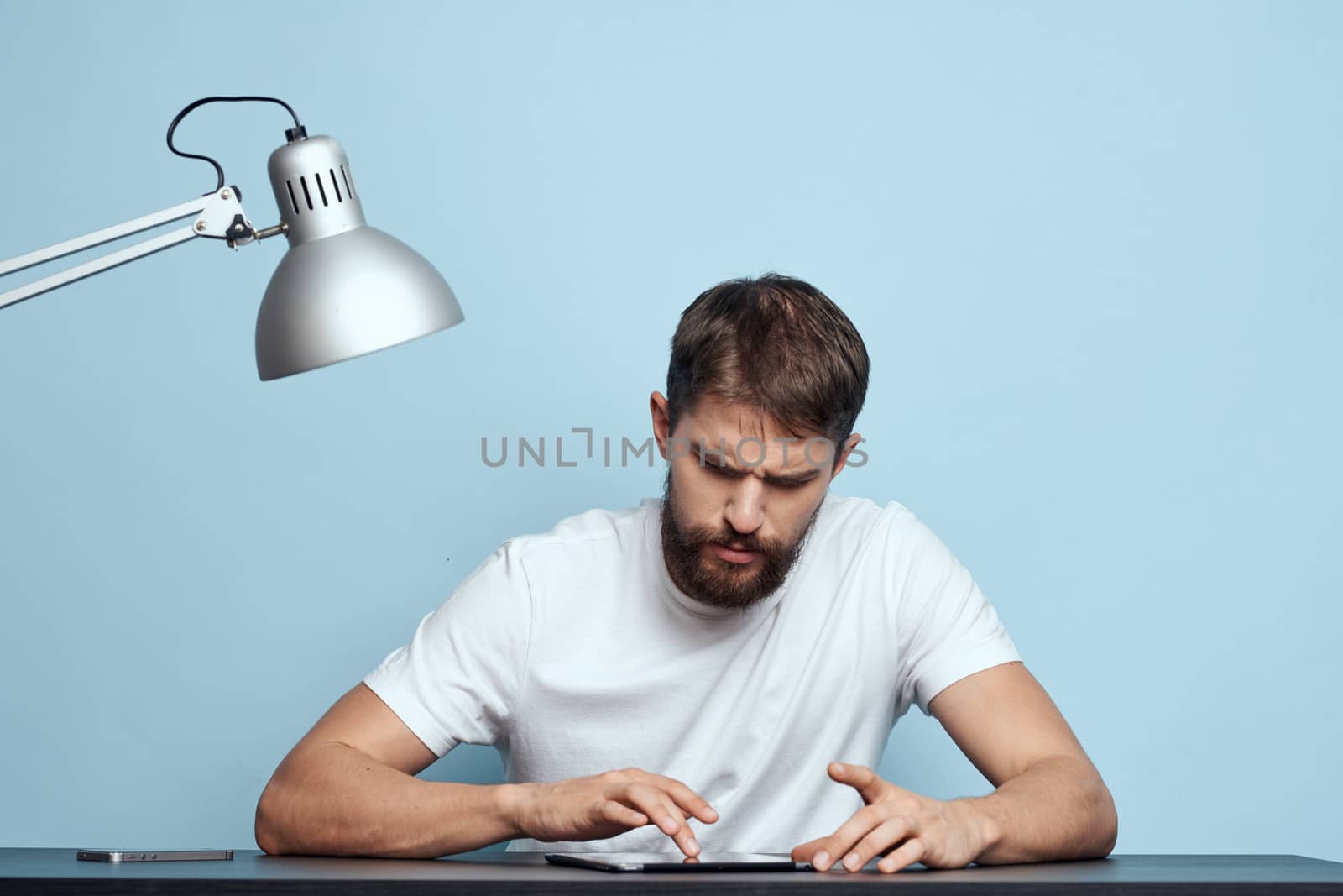 Man with tablet at table indoors and lamp work office freelancer blue background by SHOTPRIME