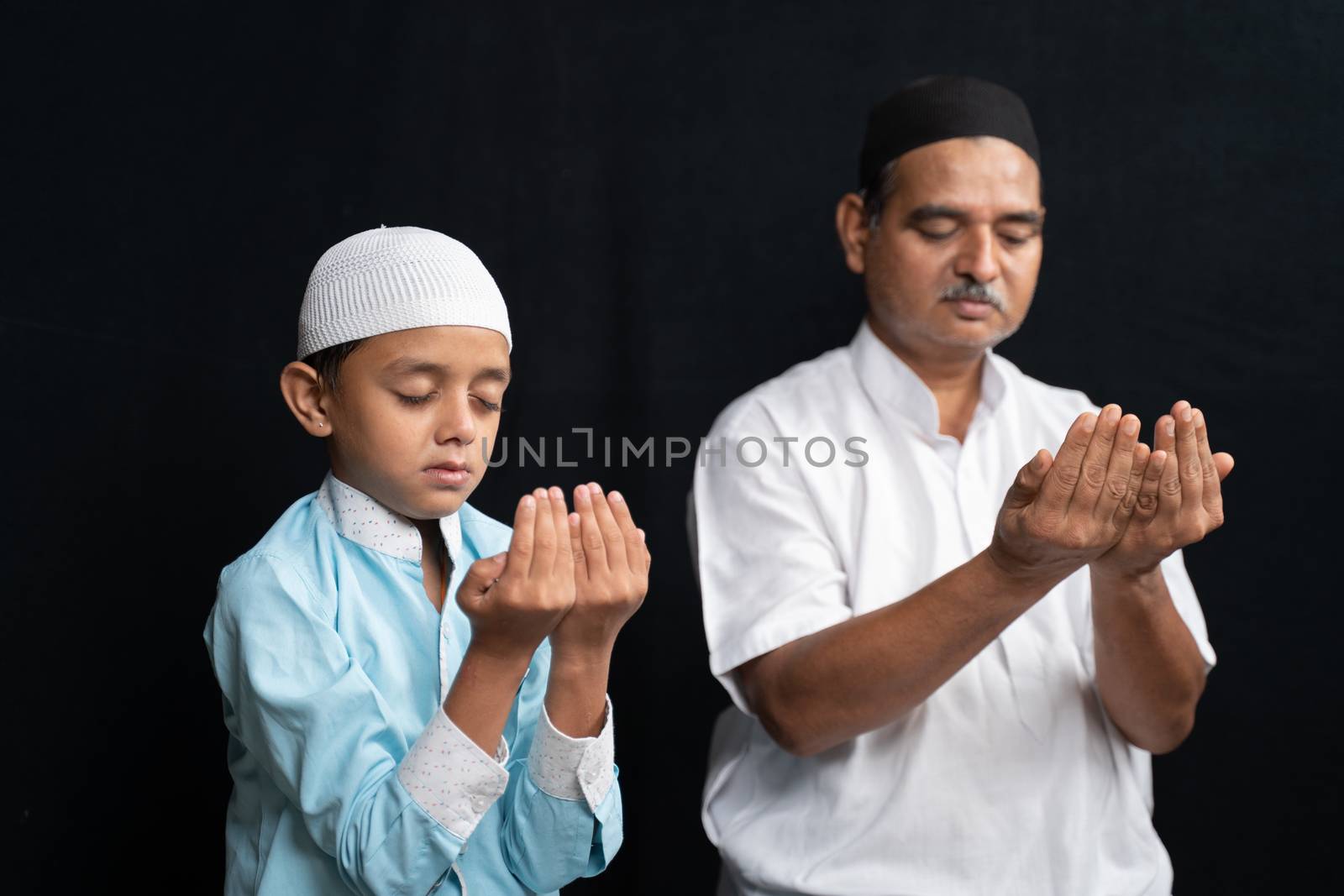 Muslim father and son in medical mask praying or performing Salah o protect from coronavirus or covid-19 by sitting
